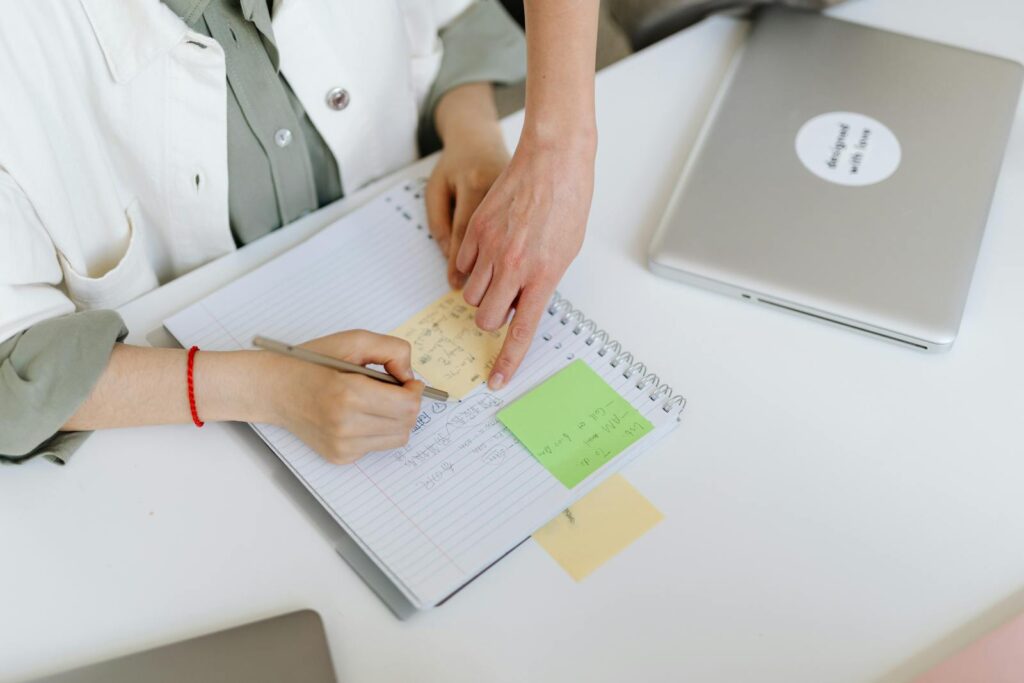 Deux personnes collaborant autour d'un carnet avec des post-it et un ordinateur portable dans un environnement de bureau.