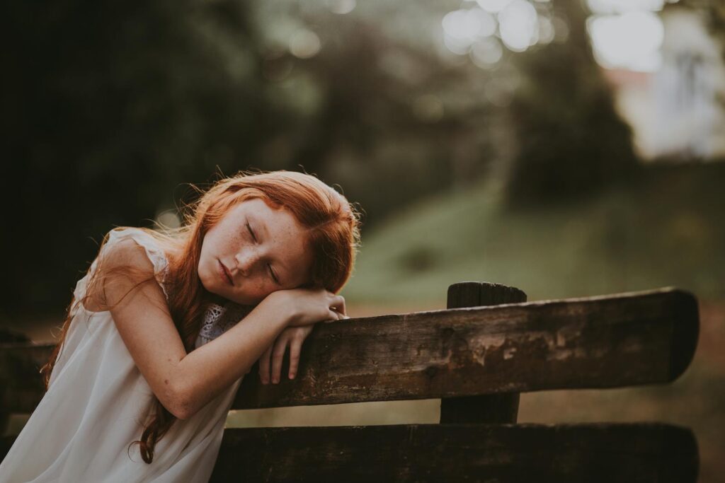 Une jeune fille dort paisiblement sur un banc en bois à l'extérieur, entourée par la nature.