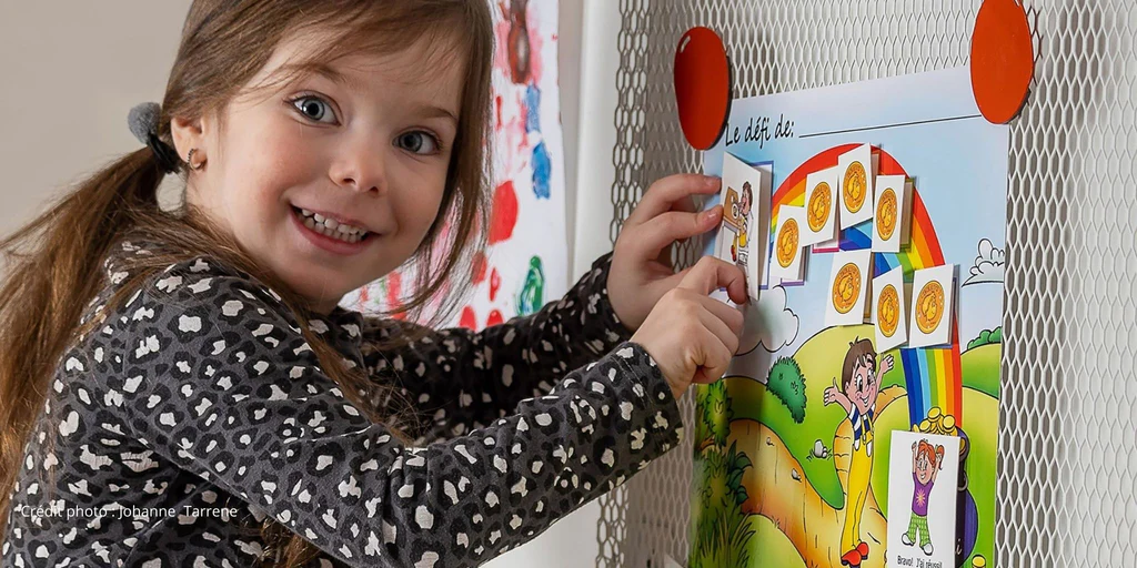 Un enfant interagissant avec un tableau de motivation collé sur un frigo.